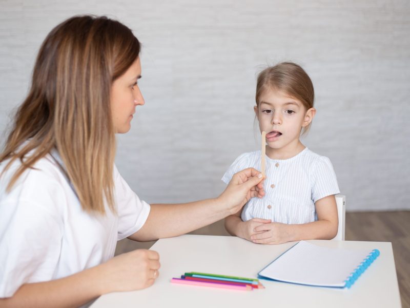 young women speech therapist and little girl training motor speech. prompts for restructuring oral muscular phonetic targets. simple ,fun ,effective speech therapy tips and materials.